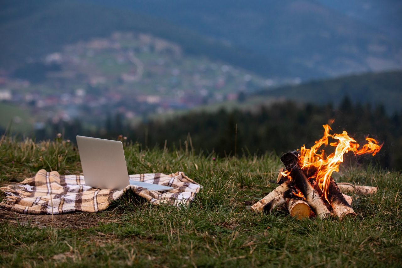 laptop laptop on plaid near campfire. behind mountain background.